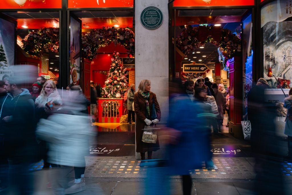 Long exposure photo of woman standing still in front of store while others pass by in a blur.