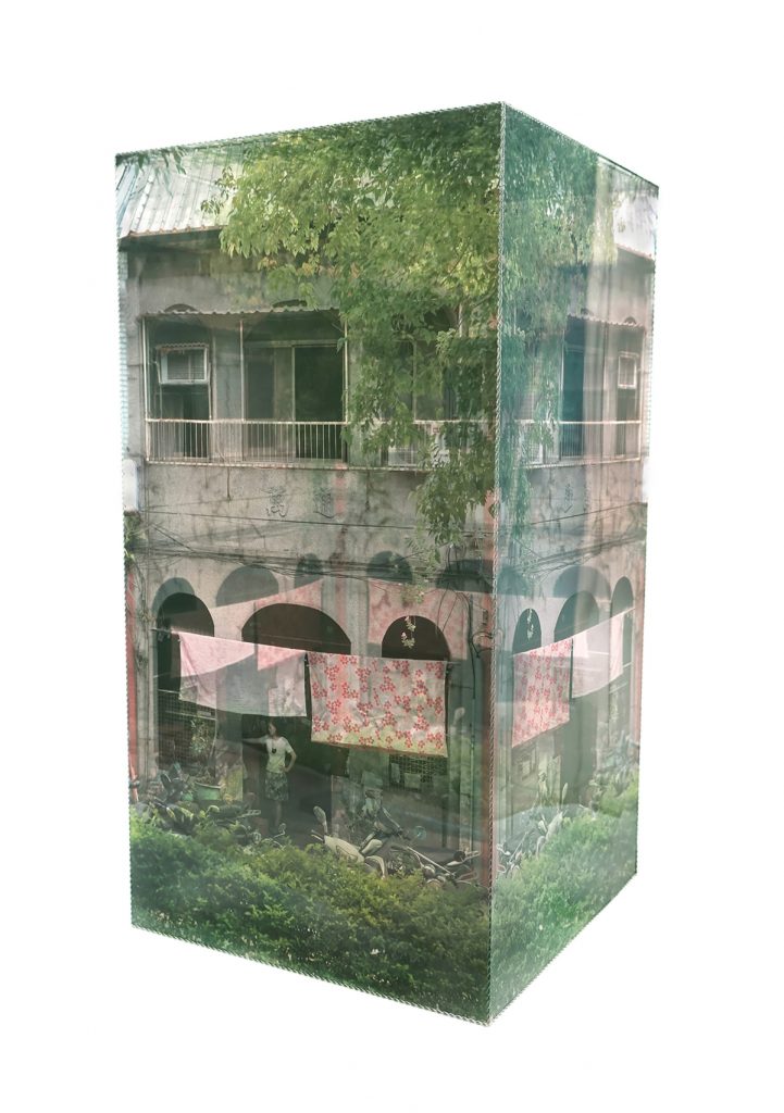 A three-dimensional layered sculpture, showing transparent panels with photographic images of buildings and people, creating a blurred sense of inside and outside space.