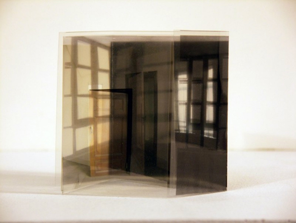 A series of folded and layered photographs arranged like small sculptural objects, where printed images overlap and curl, transforming flat photos into three-dimensional forms that blur the line between image and physical object.